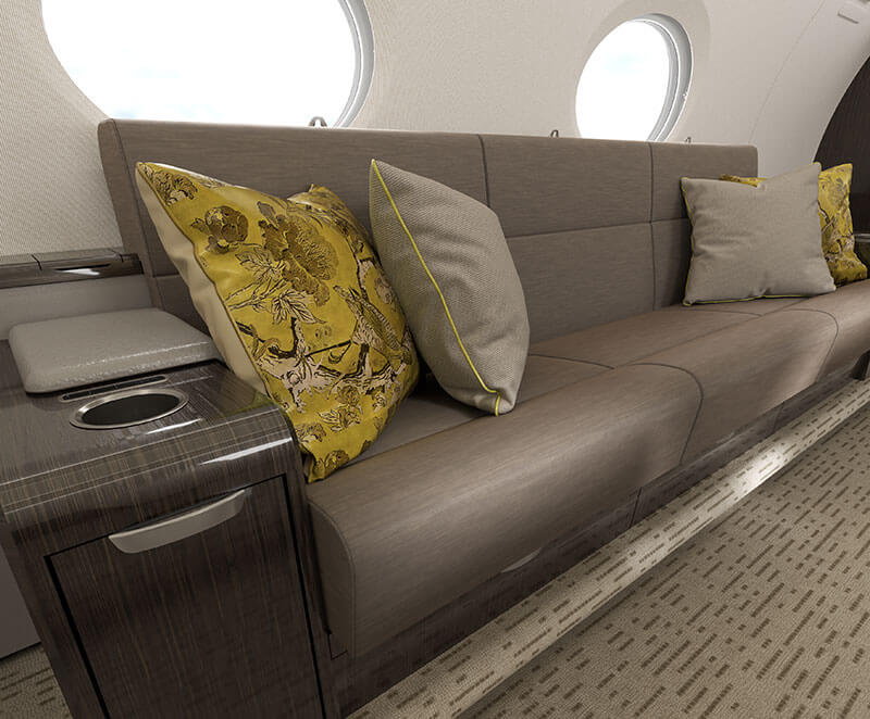 A Gulfstream G300 interior focused on a spacious divan accented with gold and tan throw pillows.
