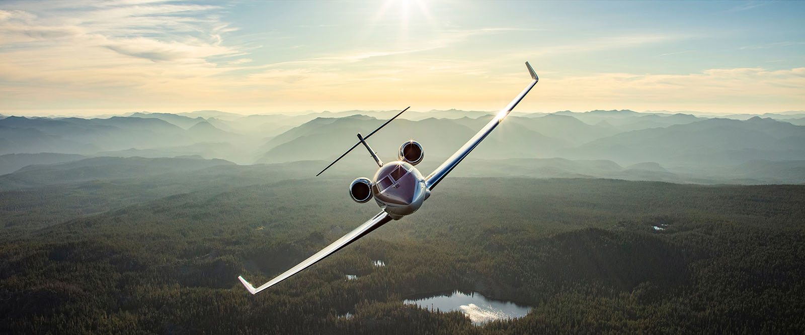 G600 banks over a forested landscape with distant mountains in morning light