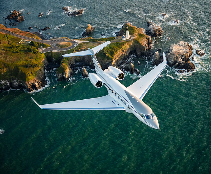 A G600 flies over a rocky coastline above emerald green water