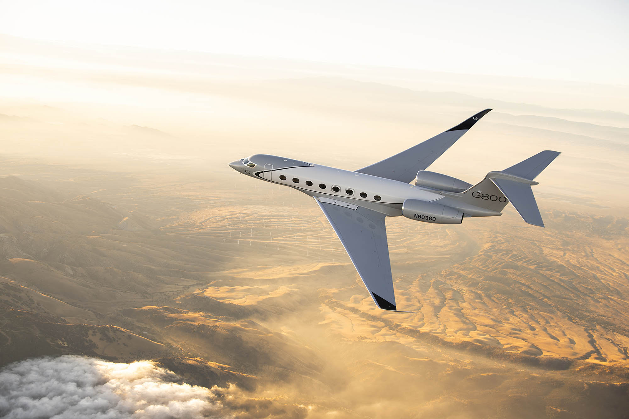 A Gulfstream G800 flies above cloud-veiled Sierra Nevada mountains.
