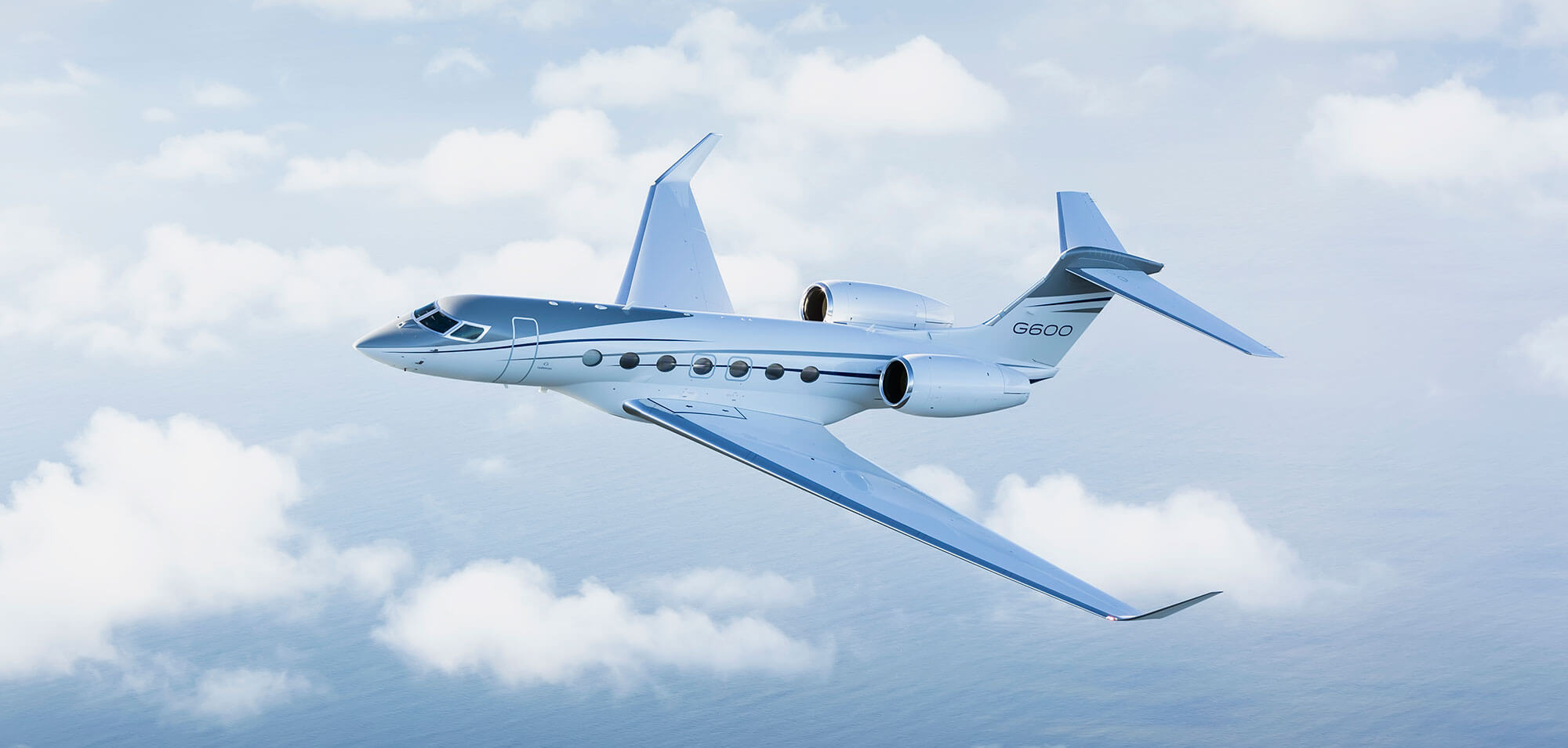 A Gulfstream G600 seen from slightly below is set against a backdrop of fluffy white clouds.