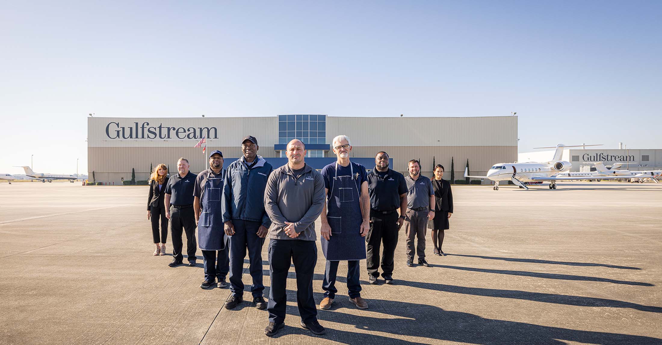 Gulfstream employees from many departments stand in formation in front of a service hangar