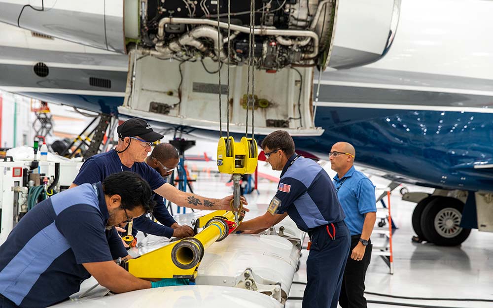 Gulfstream service center employees operate equipment in front of an aircraft being serviced.